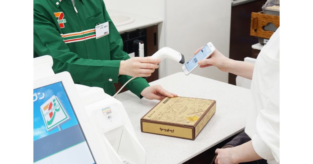 セブン-イレブンのレジで、店員が客のスマートフォンのバーコードをスキャナーで読み取っている様子。