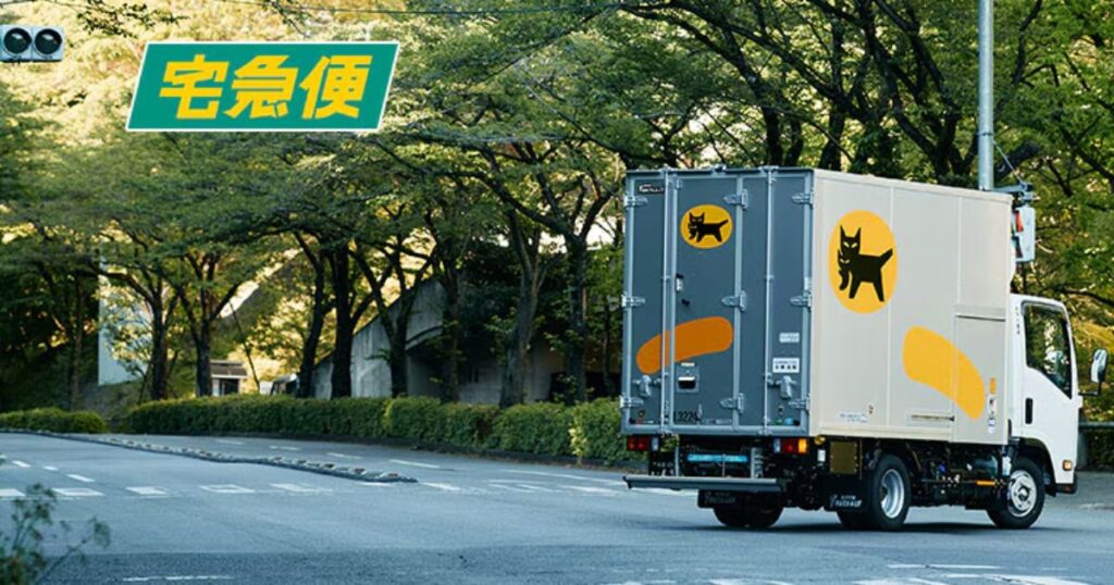 緑の並木道を走るヤマト運輸の「宅急便」配送トラックの後ろ姿。