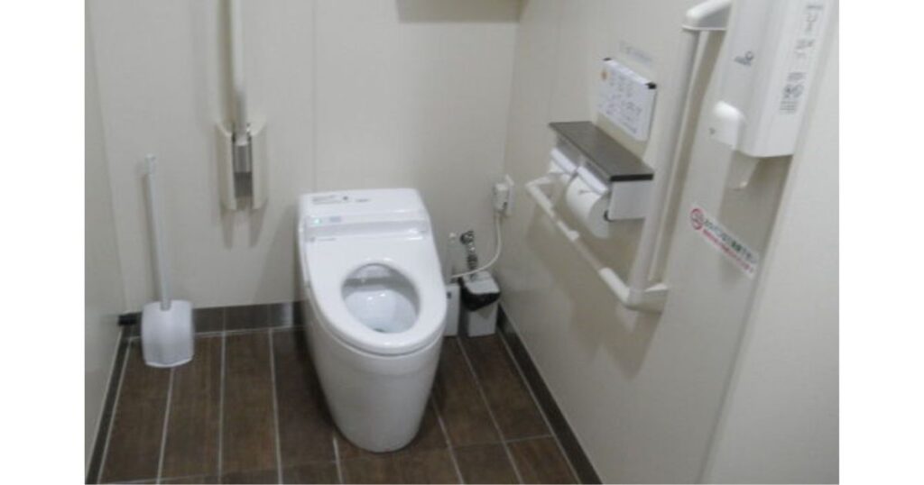 壁に手すりやペーパーホルダー、緊急呼び出しボタンが設置された、清潔なコンビニの洋式個室トイレ内の写真。