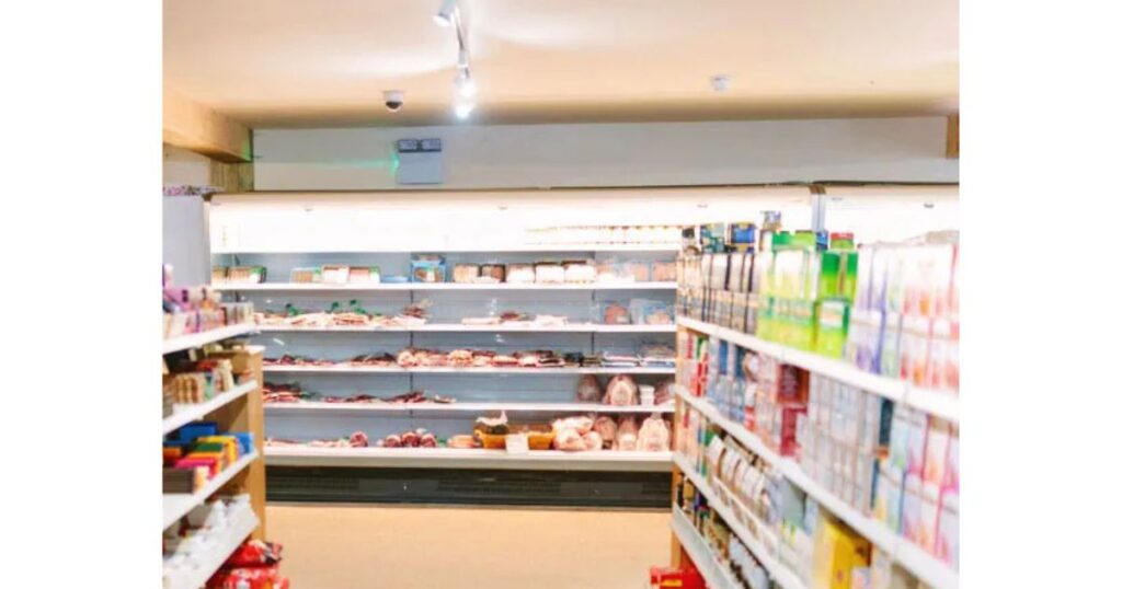明るい照明に照らされたコンビニエンスストアの店内。陳列棚にたくさんの食品や商品が並んでおり、天井近くに防犯カメラが設置されている様子。